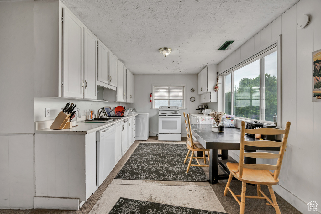 Kitchen with white appliances, washer / dryer, white cabinetry, a textured ceiling, and light countertops