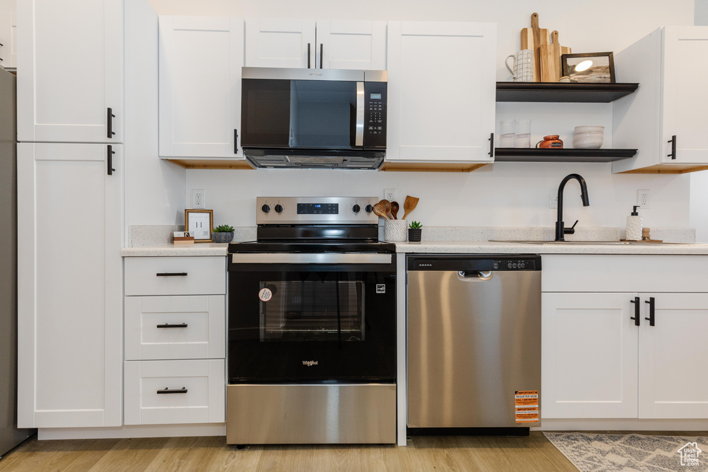 Kitchen featuring appliances with stainless steel finishes, light wood finished floors, light countertops, white cabinetry, and open shelves