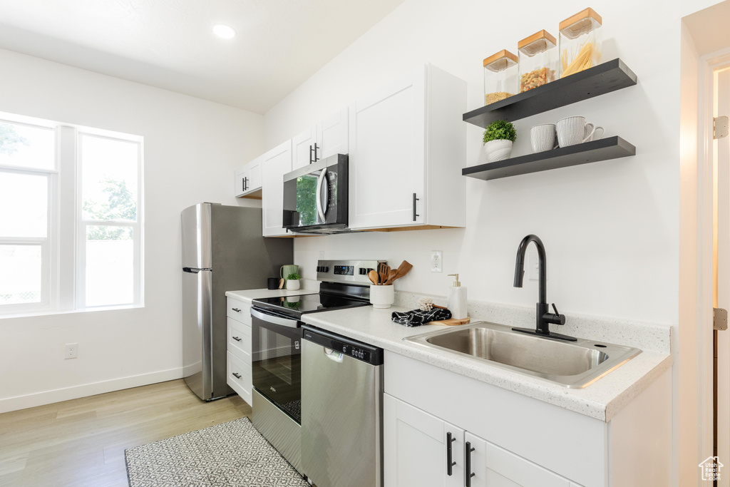 Kitchen featuring appliances with stainless steel finishes, light wood-style floors, light countertops, white cabinetry, and open shelves
