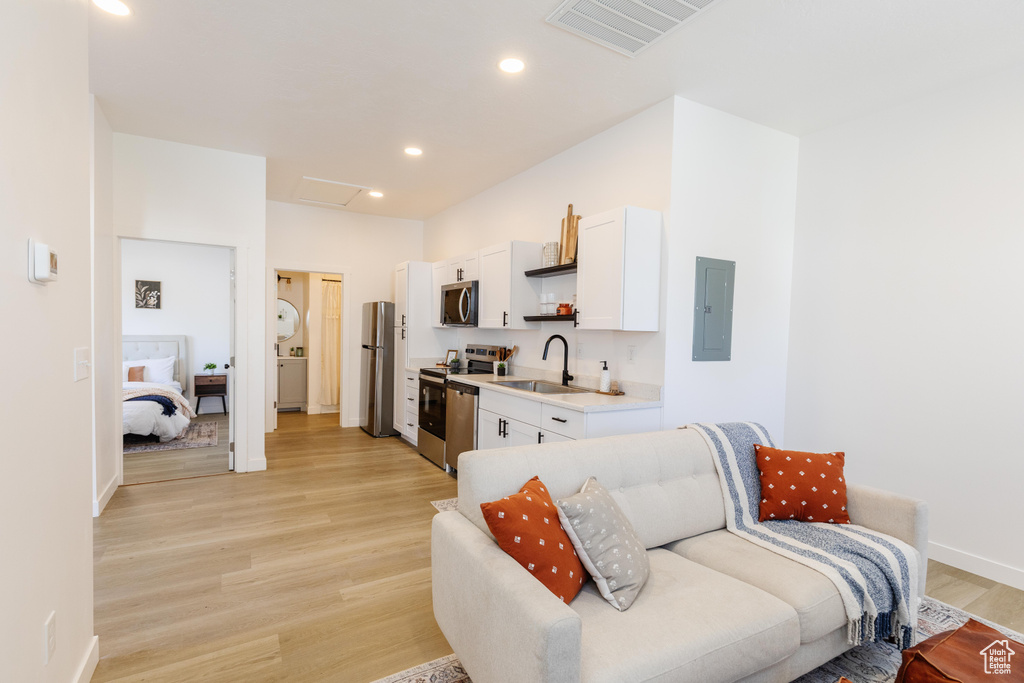 Kitchen with appliances with stainless steel finishes, electric panel, white cabinets, light wood finished floors, and light countertops