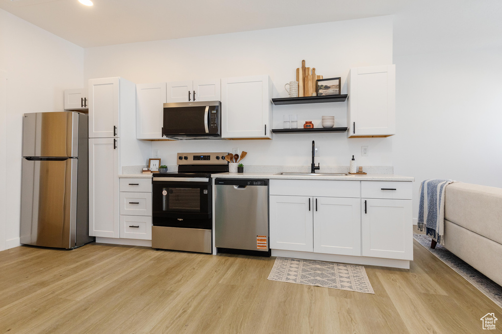 Kitchen featuring appliances with stainless steel finishes, light wood-style floors, light countertops, white cabinetry, and open shelves