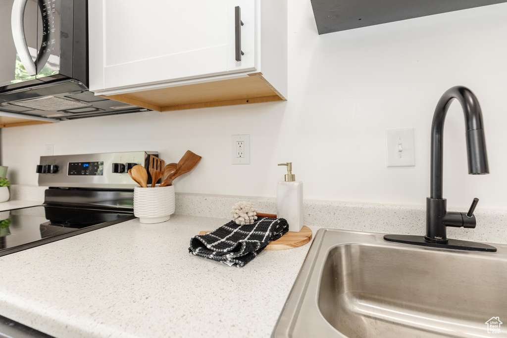 Kitchen featuring stainless steel electric range oven, white cabinetry, and light stone counters