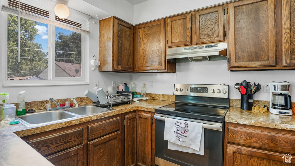 Kitchen with stainless steel range with electric stovetop, under cabinet range hood, light countertops, and brown cabinetry