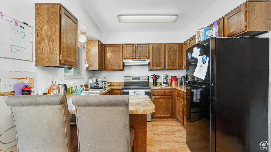 Kitchen with freestanding refrigerator, under cabinet range hood, stainless steel electric range, a peninsula, and light wood finished floors