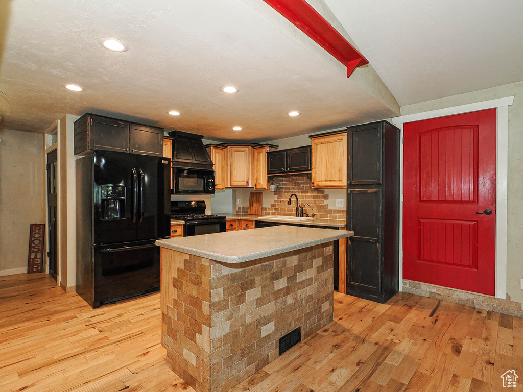 Kitchen featuring black appliances, light wood finished floors, light countertops, a kitchen island, and tasteful backsplash