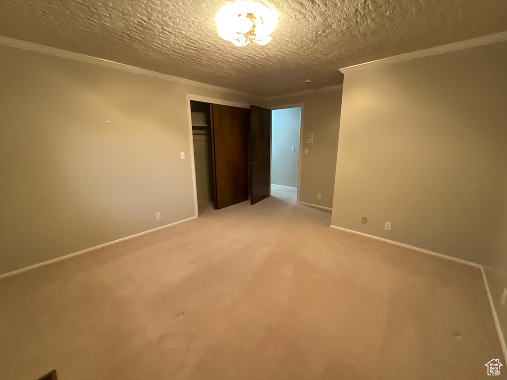 Unfurnished bedroom featuring a closet, a textured ceiling, light colored carpet, and ornamental molding