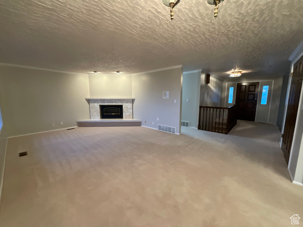 Unfurnished living room featuring a textured ceiling, carpet flooring, a fireplace with raised hearth, and crown molding