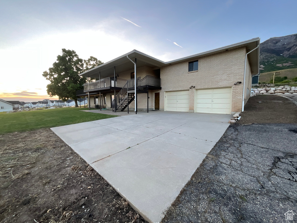Back of house with an attached garage, concrete driveway, a lawn, a wooden deck, and brick siding