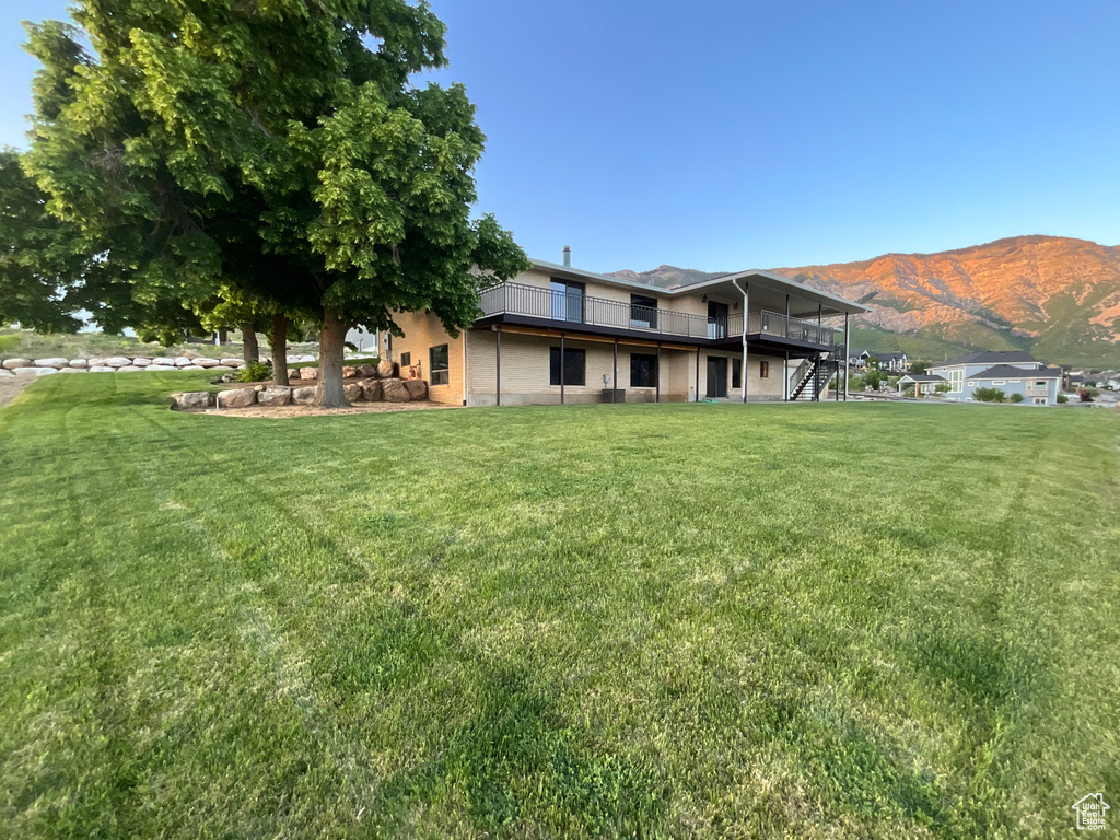 Back of property featuring a yard, a deck with mountain view, and stairs