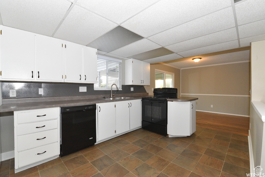 Kitchen featuring black appliances, a peninsula, dark countertops, white cabinetry, and a paneled ceiling