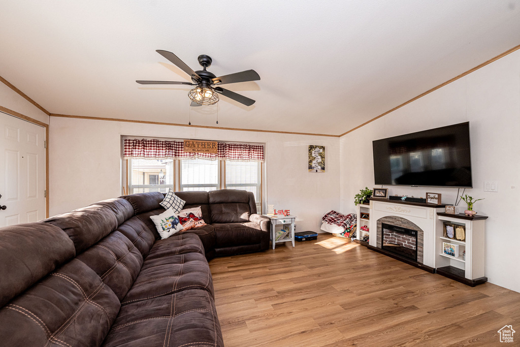 Living room with ornamental molding, ceiling fan, vaulted ceiling, light wood finished floors, and a fireplace