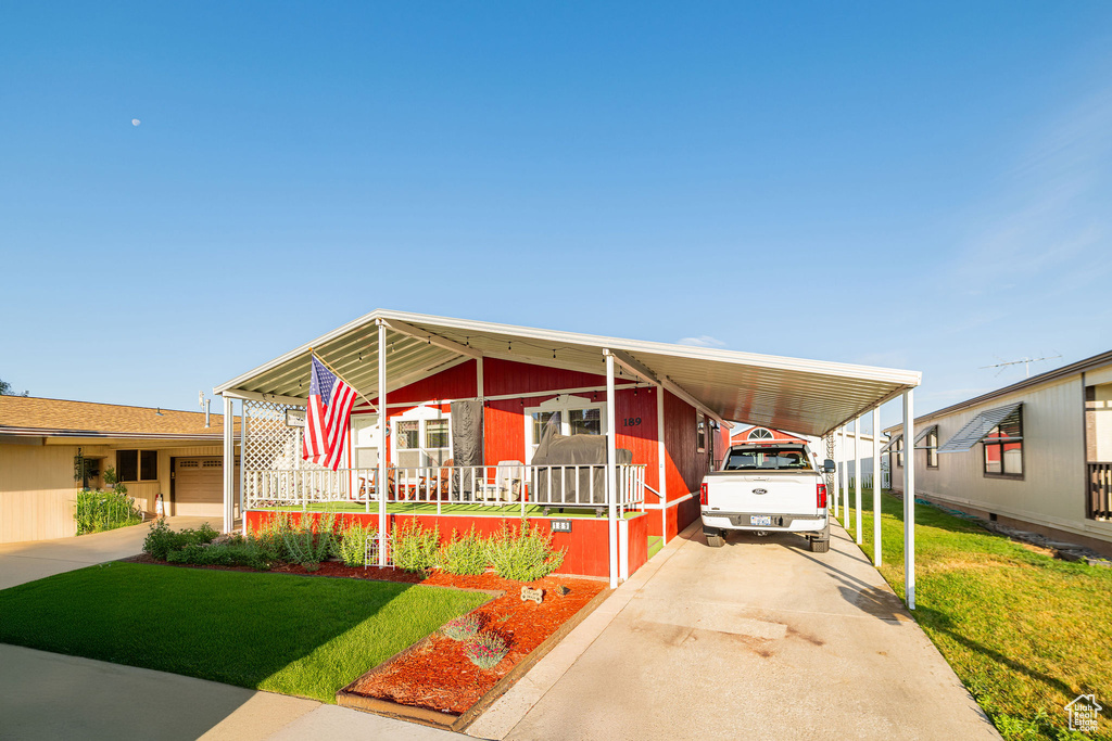 Manufactured / mobile home with concrete driveway, a front lawn, an attached carport, and covered porch