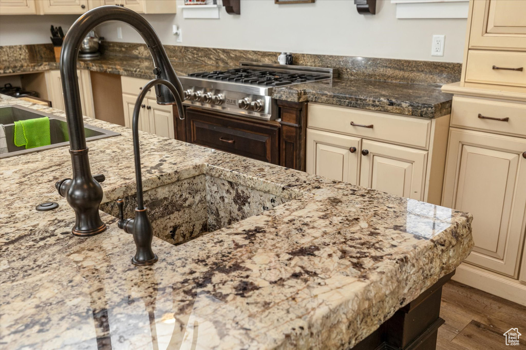 Kitchen with cream cabinetry, stainless steel gas stovetop, wood finished floors, and light stone countertops