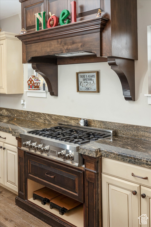 Kitchen featuring cream cabinets, stainless steel gas cooktop, light wood-type flooring, and dark stone countertops
