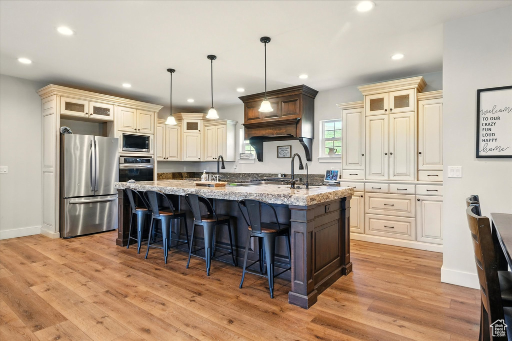Kitchen with appliances with stainless steel finishes, cream cabinetry, a large island with sink, light wood-style flooring, and recessed lighting