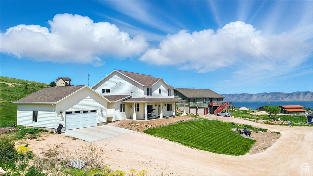 View of front of house with driveway, covered porch, an attached garage, a mountain view, and a front lawn