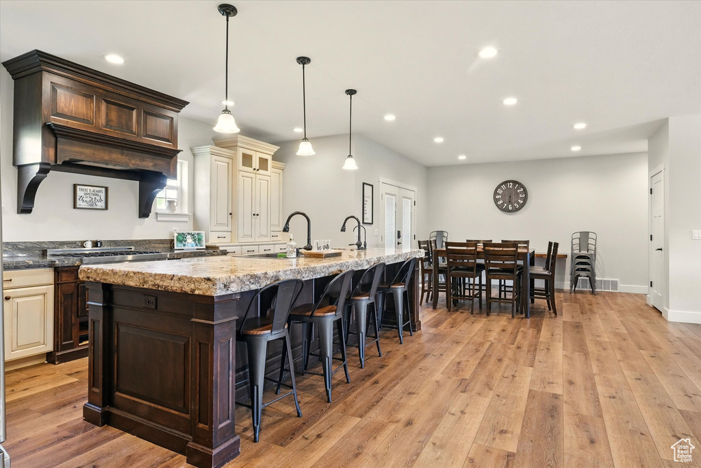 Kitchen with cream cabinetry, light stone countertops, recessed lighting, a breakfast bar area, and a kitchen island with sink
