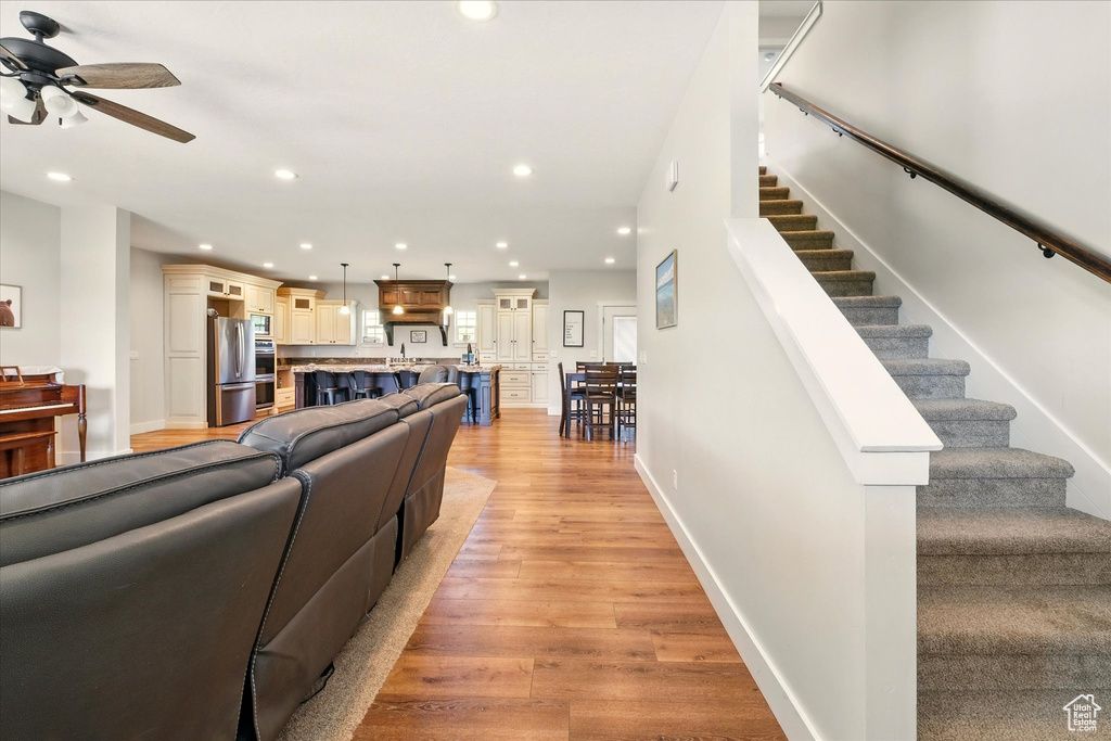 Living room with ceiling fan, light wood finished floors, recessed lighting, and stairs