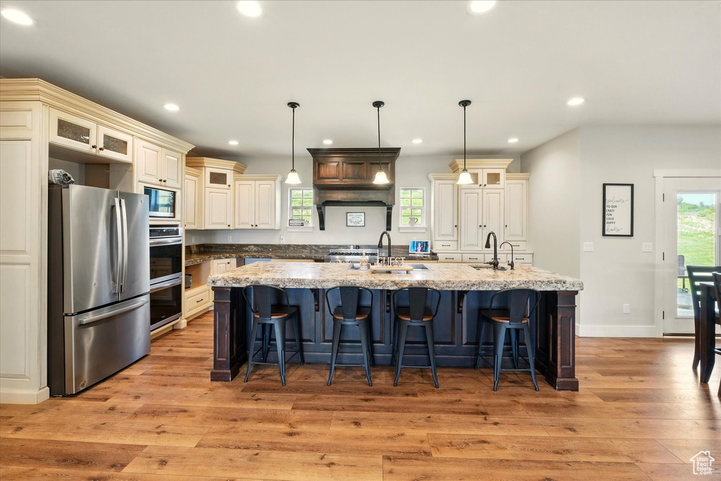 Kitchen with appliances with stainless steel finishes, cream cabinetry, light wood-type flooring, a large island, and recessed lighting