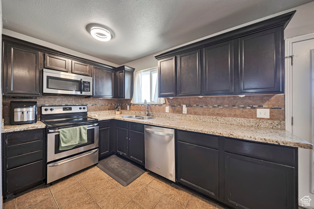 Kitchen with stainless steel appliances, backsplash, light stone counters, a textured ceiling, and light tile patterned flooring