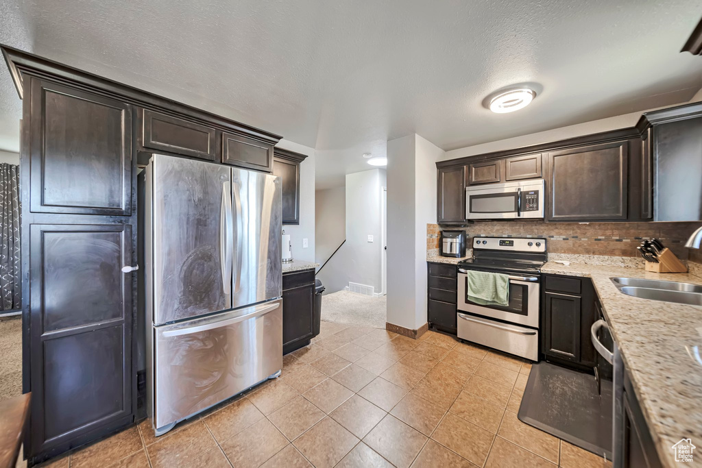 Kitchen with stainless steel appliances, backsplash, dark brown cabinets, and light tile patterned flooring