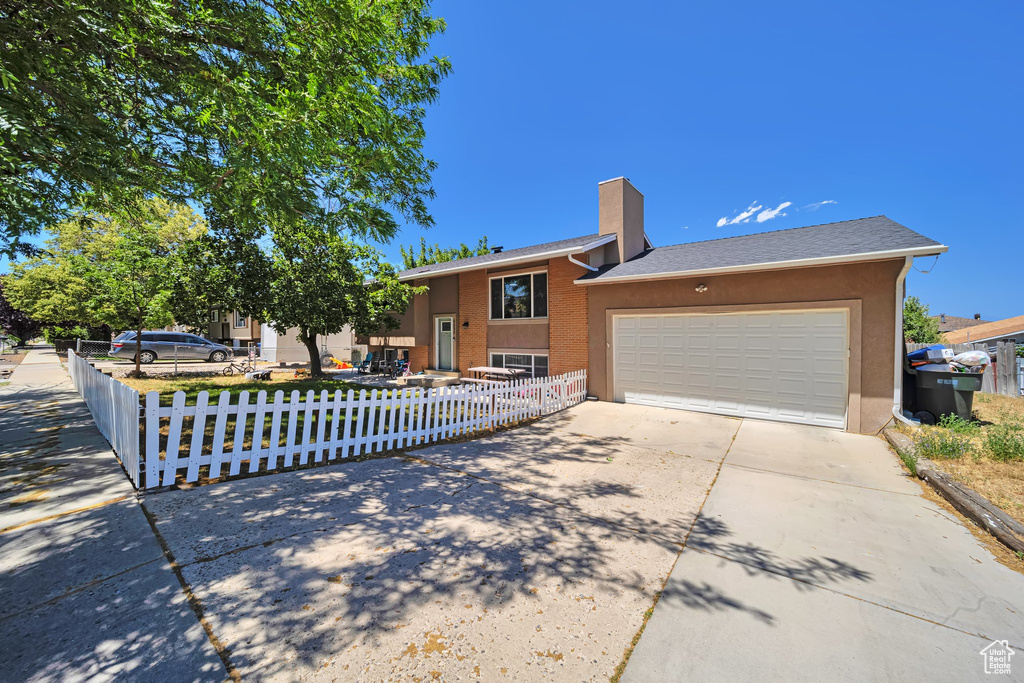 View of front of house with driveway, a fenced front yard, a chimney, a garage, and stucco siding