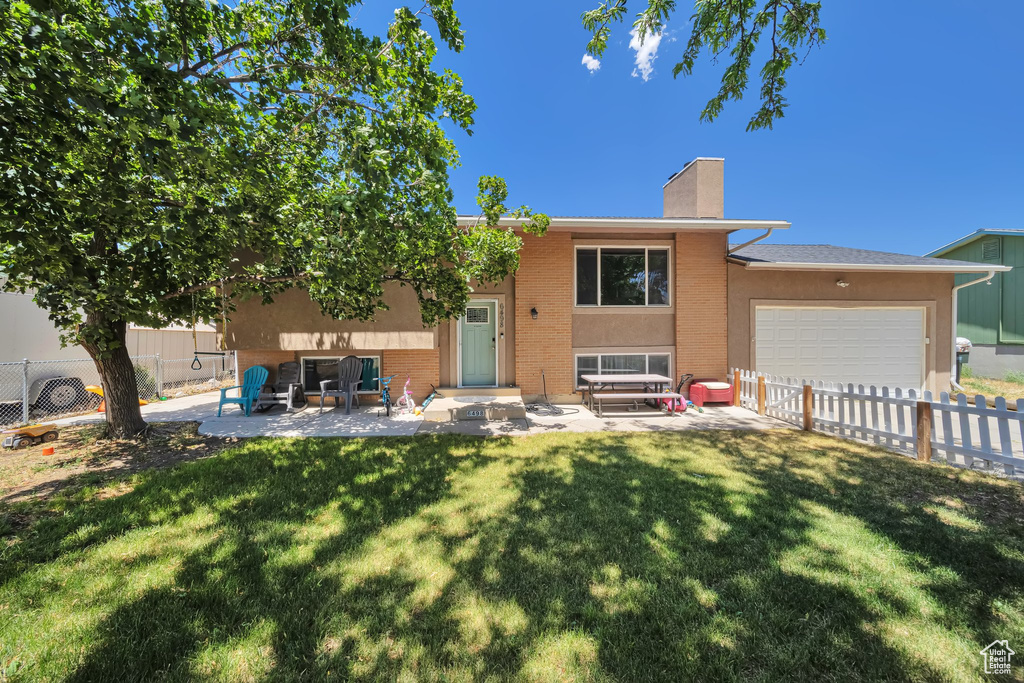 Back of property with a chimney, brick siding, an attached garage, and a patio area