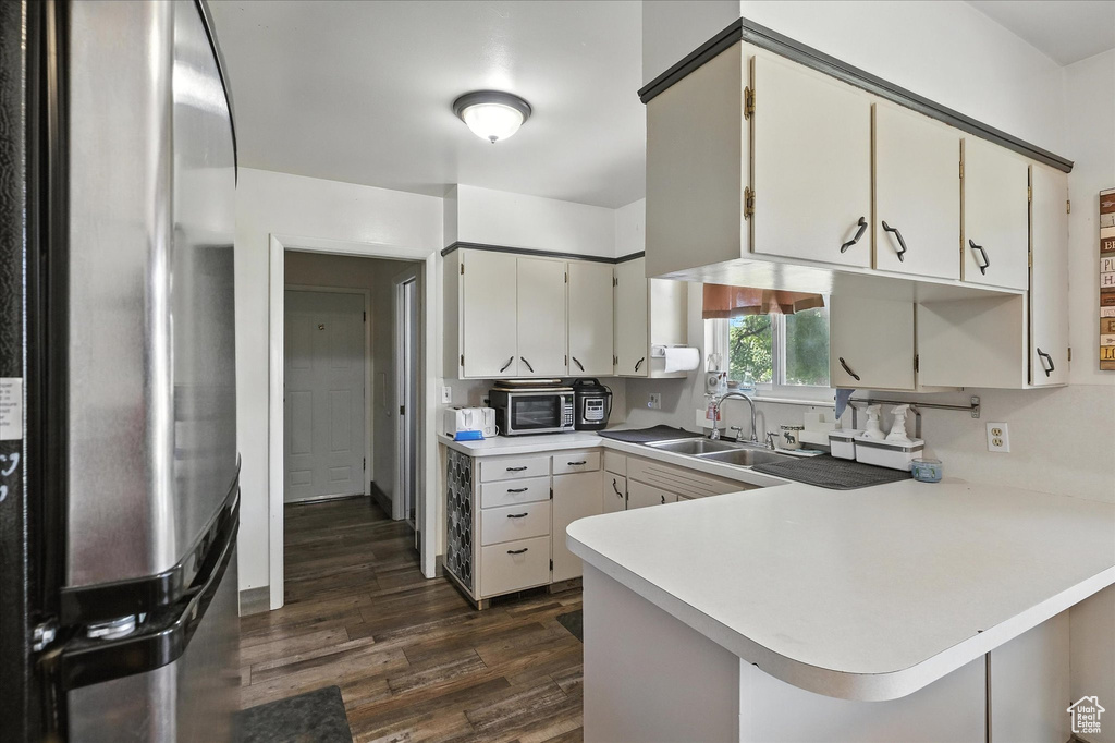 Kitchen featuring freestanding refrigerator, light countertops, dark wood-style flooring, a peninsula, and stainless steel microwave