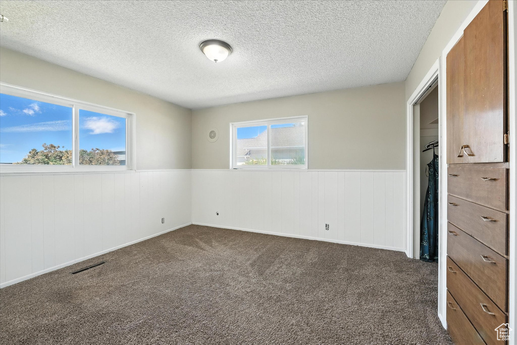 Unfurnished bedroom featuring a wainscoted wall, a textured ceiling, and dark carpet