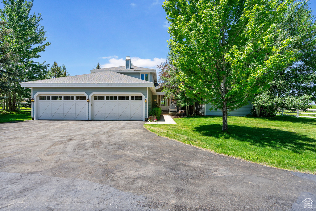 View of front facade with a front yard, asphalt driveway, an attached garage, a chimney, and roof with shingles