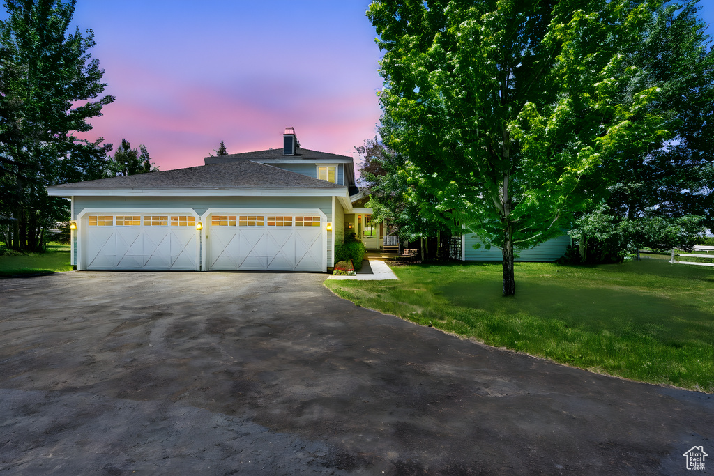 View of front of home with a yard, asphalt driveway, an attached garage, and a chimney