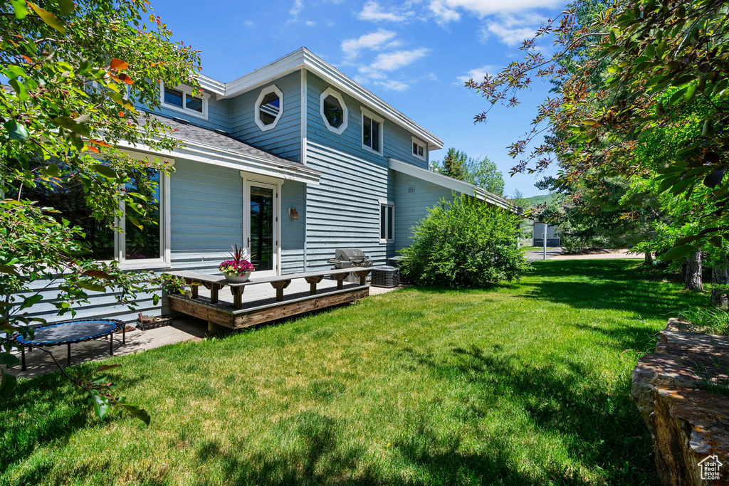 Rear view of house with a yard, a wooden deck, and roof with shingles