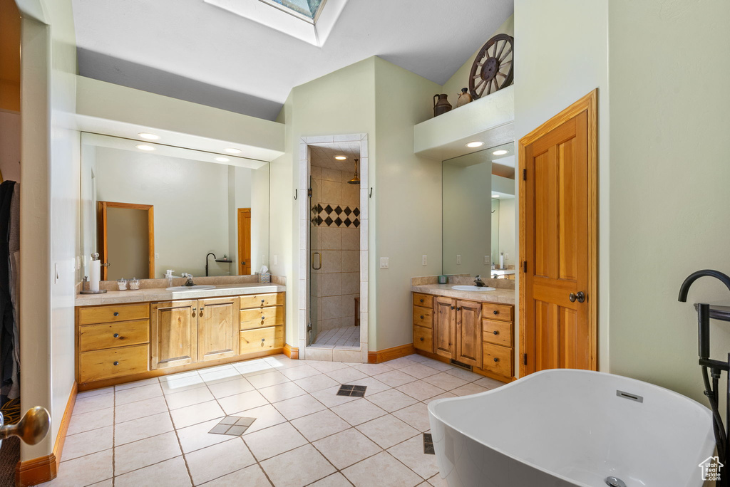 Bathroom featuring a skylight, a stall shower, vaulted ceiling, a freestanding bath, and two vanities