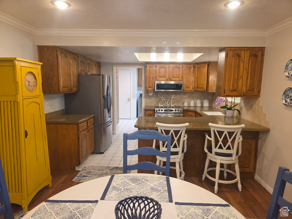 Kitchen with appliances with stainless steel finishes, a peninsula, tasteful backsplash, brown cabinetry, and light wood finished floors