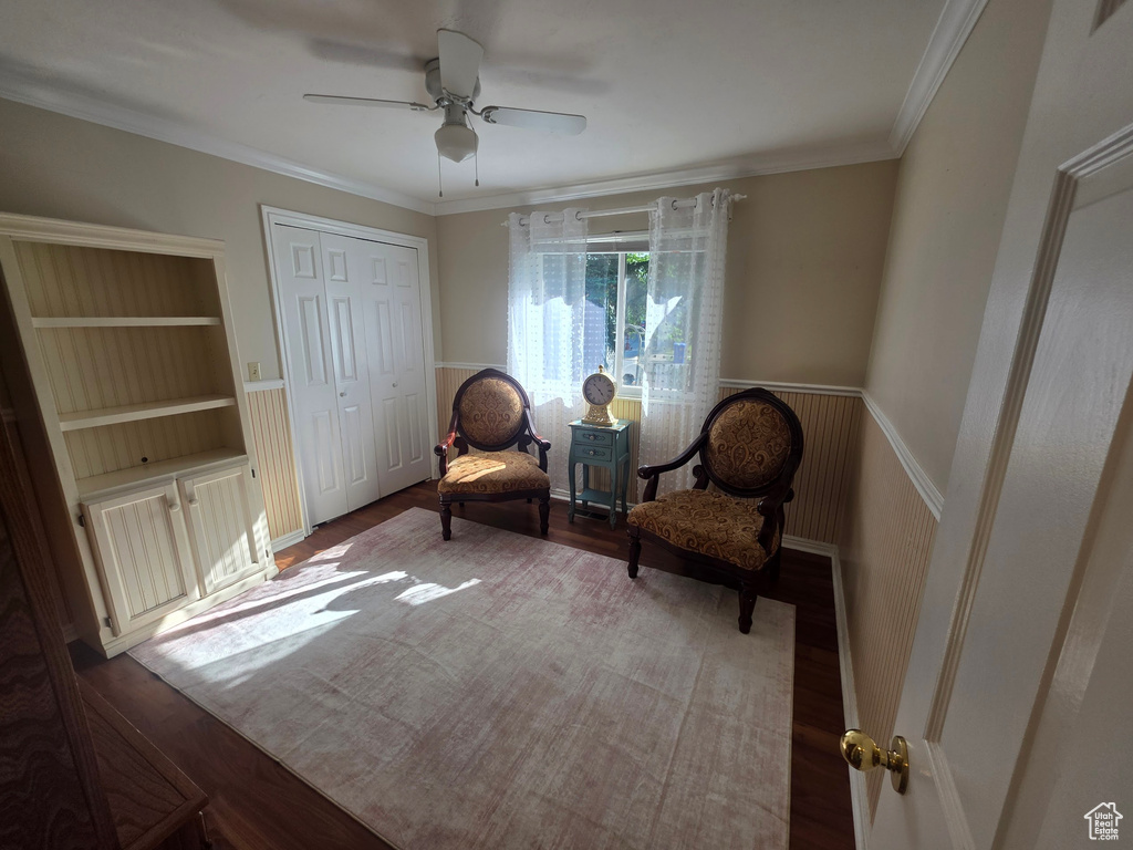 Sitting room featuring wood finished floors, a ceiling fan, crown molding, and wainscoting
