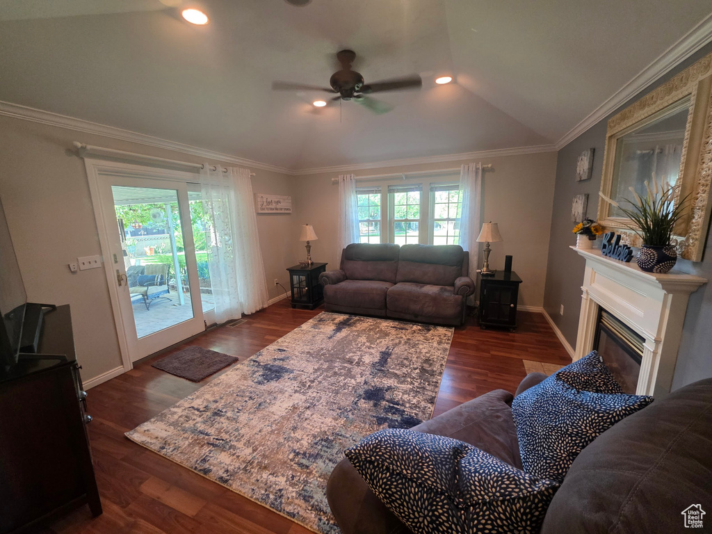Living room with vaulted ceiling, ceiling fan, a glass covered fireplace, dark wood-style flooring, and crown molding