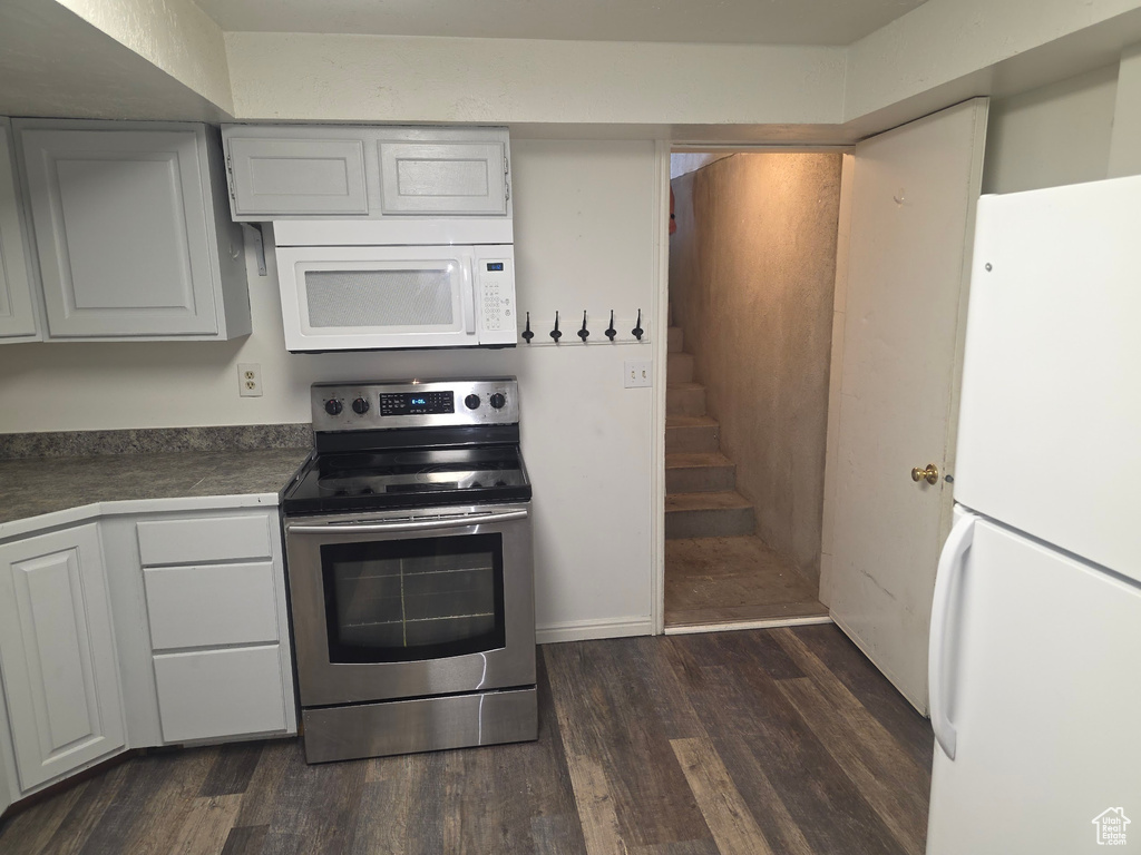 Kitchen with white appliances, dark wood-style floors, and dark countertops