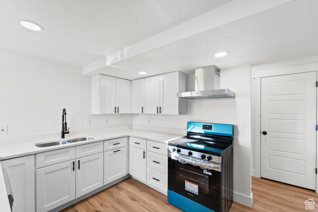 Kitchen featuring wall chimney exhaust hood, stainless steel electric range oven, light wood-style flooring, white cabinets, and recessed lighting