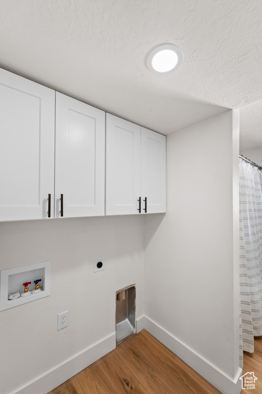 Laundry room with cabinet space, hookup for an electric dryer, light wood-style floors, washer hookup, and a textured ceiling