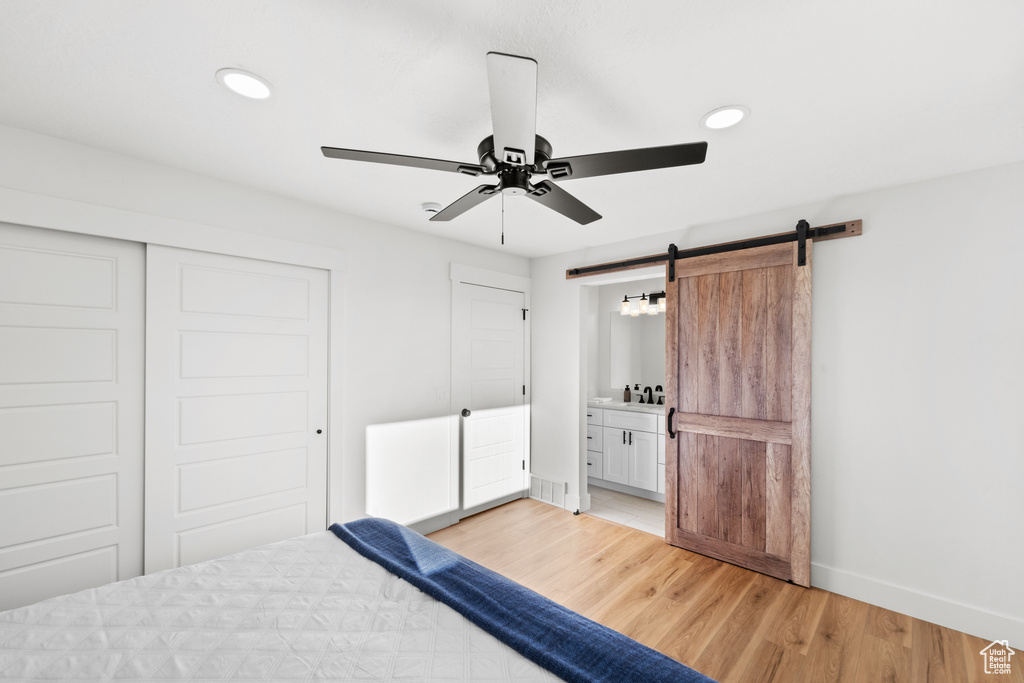 Unfurnished bedroom featuring a barn door, light wood finished floors, a closet, recessed lighting, and connected bathroom
