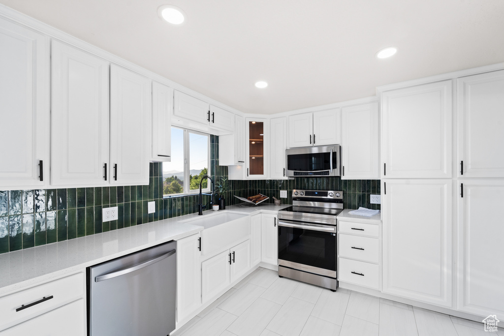 Kitchen with stainless steel appliances, white cabinetry, backsplash, light countertops, and recessed lighting
