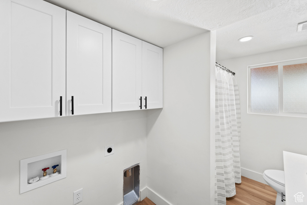 Laundry area with wood finished floors, hookup for an electric dryer, cabinet space, a textured ceiling, and washer hookup
