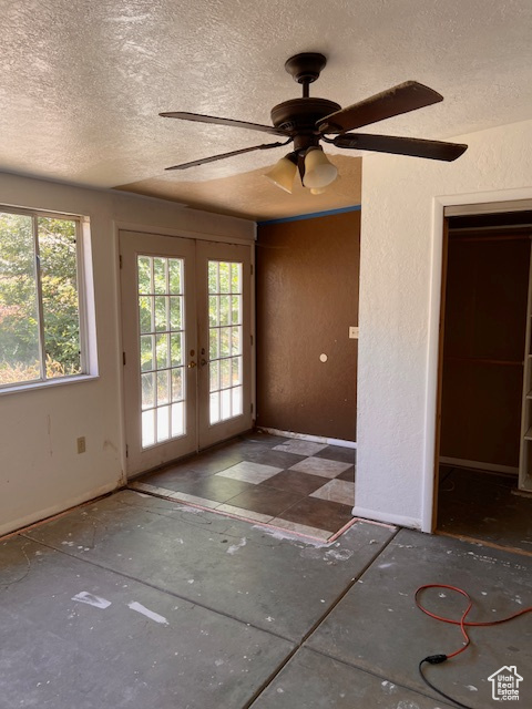 Spare room featuring french doors, plenty of natural light, a textured ceiling, a ceiling fan, and a textured wall
