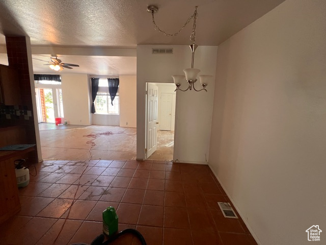 Unfurnished dining area with a chandelier, a ceiling fan, and a textured ceiling
