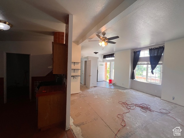Unfurnished living room with a ceiling fan and a textured ceiling