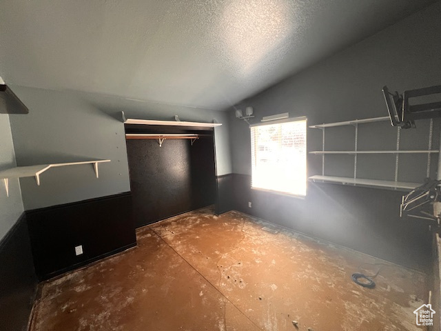 Unfurnished bedroom with vaulted ceiling, a textured ceiling, and a closet