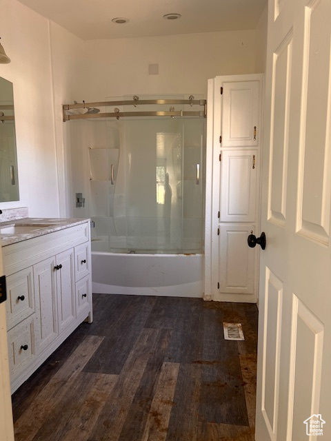 Full bath with wood finished floors, vanity, and combined bath / shower with glass door