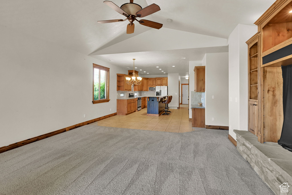 Unfurnished living room featuring a chandelier, light colored carpet, ceiling fan, lofted ceiling, and light tile patterned flooring
