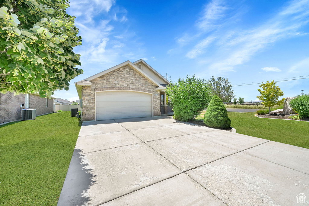 View of front of house with concrete driveway, a front yard, an attached garage, and stone siding