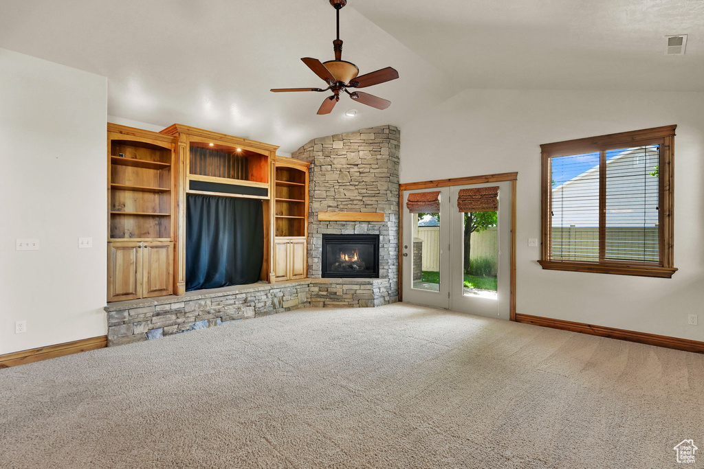 Unfurnished living room with a ceiling fan, lofted ceiling, carpet flooring, and a stone fireplace
